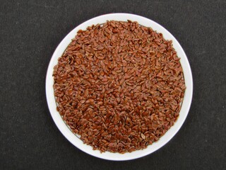 Flax seeds in a plate on black background 