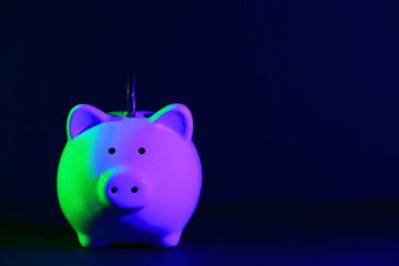 Piggy bank on a dark background with coin and green-purple backlight. Banking concept. Bright neon lights
