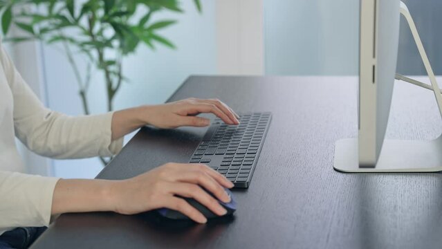 Close-up of a woman's hand using a desktop computer in the office.