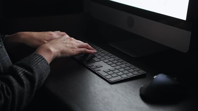 Scene of an anonymous person using a computer in a dark room.