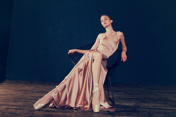 portrait of a ballerina in a pink dress is sitting on a chair with her leg in the slit of the dress
