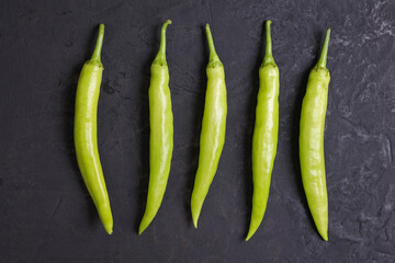 Long green chili peppers on black stone background
