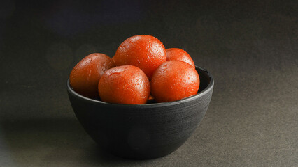 Sweet Gulab Jamun served in black ceramic bowl, Famous Indian dessert sweets isolated over black indoor studio background