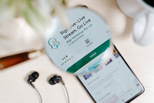 Bigo Live online streaming platform mobile app in Google Play online store on smartphone screen on table, view through magnifying glass. Smolensk, Russia 02.12.2022