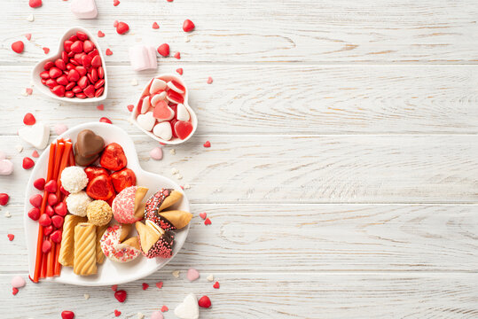 Valentine's Day celebration concept. Top view photo of heart shaped saucers with chocolate jelly candies and cookies on white wooden desk background with copyspace
