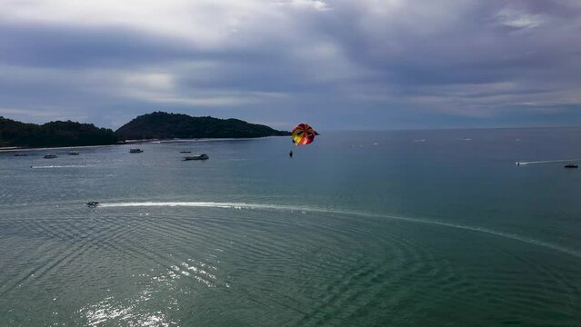 Parasailing in Phuket. A long shot of a man flying in the sky with help of colorful parasail wing or Parachute on a bright sunny day at beach