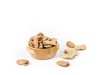 Fava beans scattered around a ceramic bowl isolated over white