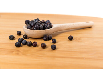 Dried juniper berries scattered around a wood spoon over wood board side view