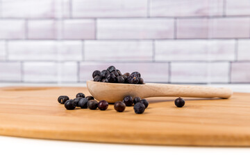 Dried juniper berries scattered around a wood spoon over wood board side view