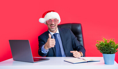 glad mature man wear red santa claus hat and party glasses in business office. thumb up