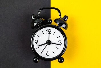 A Black vintage alarm clock on yellow background with empty space for your text or message.