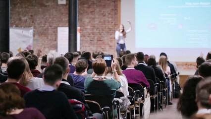 Speaker at conference make a poll from the scene. Business and Entrepreneurship concept. Audience at the conference hall. Professor woman provide a lecture in auditorium class.