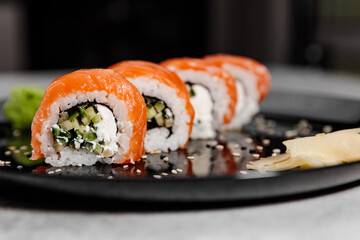 Four portions of sushi with salmon and cucumber with vossabi sauce and ginger on a black plate.Close-up
