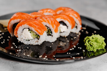 Eight portions of sushi with salmon and cucumber with vossabi sauce and ginger on a black plate.Close-up
