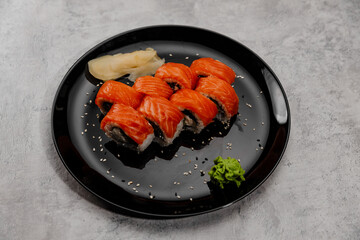 Eight servings of salmon and cucumber sushi with vossabi sauce and ginger on a black plate. 