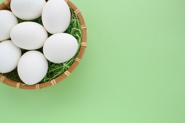Fresh chicken eggs in wooden rattan wicker basket on green background. Natural healthy nutrition organic farm food product concept. World egg day, easter holiday composition. Close-up, flatlay