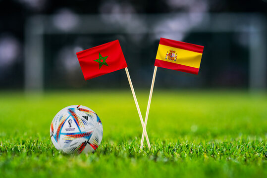 QATAR, DOHA, DECEMBER 2. 2022: Morocco - Spain Round of 16 football match. Official ball of Fifa world cup Qatar 2022 on green grass. Soccer stadium in background. Handmade national flags.