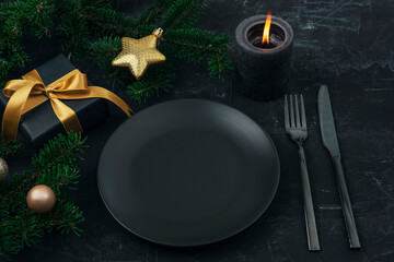 Christmas, New Year table setting in black. Black plate, fork, knife, fir tree, candle, gift box and toys. Top view, mockup