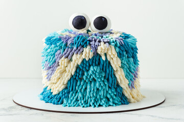 Cute monster cake on the white background. Funny birthday cake with turquoise and blue fluffy cream...