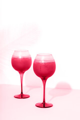Viva magenta cocktail with ice in wineglasses on a pink table, tropical palm leaf shadow on the background