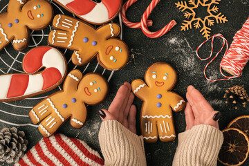 Woman hands hold decorated gingerbread man with white icing. Homemade traditional festive Christmas cookies. Flat lay. Winter holidays background. Merry Christmas and Happy New Year