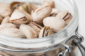 Close up of pistachio nut seeds in a glass jar on the white background. Salted dried beer snack....