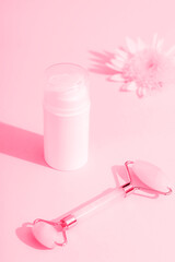Obraz na płótnie Canvas White cosmetic bottle, flower and facial roller on pink background in sunlight. Skincare, spa and wellness concept