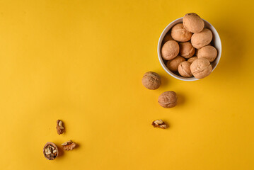 Top view of walnuts in a  bowl on a bright yellow plain background with copy space