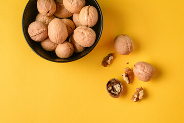 Top view of walnuts in a blаk bowl on a bright yellow plain background wiht copy space for text