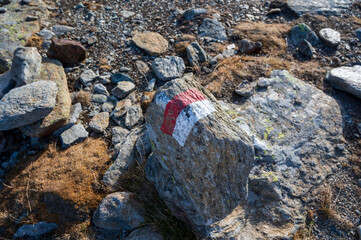 Red and white tourist sign on rock high in the mountains.