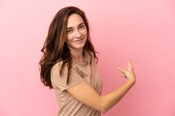 Young caucasian woman isolated on pink background pointing back