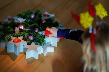 Hand of child lighting a candle on advent wreath on Christmas eve or first advent. Tradtional...