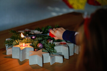 Naklejka na ściany i meble Hand of child lighting a candle on advent wreath on Christmas eve or first advent. Tradtional wreath in Germany. Happy child celebrating family holiday