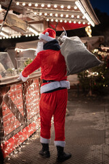 Portrait von einem verkleideten Weihnachtsmann, der auf einem Weihnachtsmarkt von Lichtern umgeben...