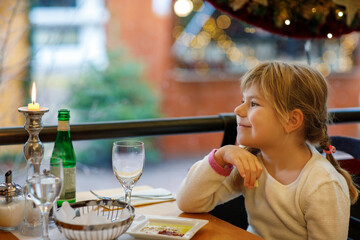 Little preschool girl sitting in restaurant near window decorated for Christmas. Child waiting for food. Happy family time