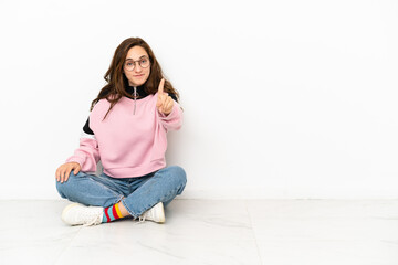 Young caucasian woman sitting on the floor isolated on white background showing and lifting a finger