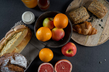 Bread, croissants, rolls, homemade yogurt, marmalade and honey jars, oranges, apples and sliced ​​grapefruit on the table in a rustic wooden bowl and wooden plate