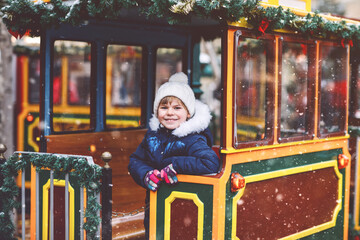 Little preschool girl on a carousel train at Christmas funfair or market, outdoors. Happy child...
