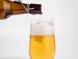 Fresh beer is poured from a bottle into a glass. Beer on a white background.