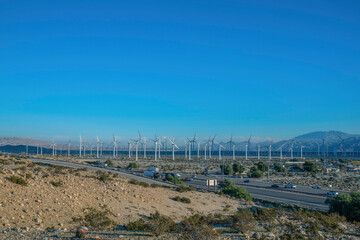 Windmills along road with cars against mountain and blue sky background