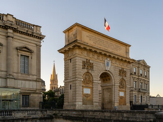 Early morning view of historic Porte du Peyrou arch of triumph with French flag and St Anne church...