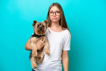 Young Lithuanian woman holding a dog isolated on blue background with sad expression