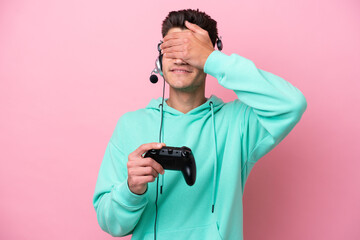 Young handsome caucasian man playing with a video game controller isolated on pink background covering eyes by hands. Do not want to see something