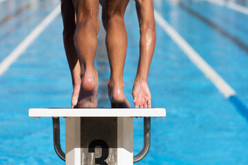 Swimmer in low position on starting block in a swimming pool