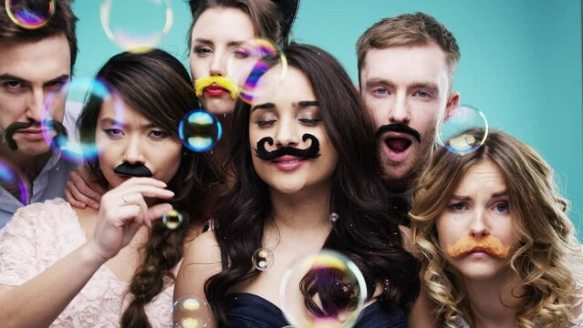 Friends, group and photobooth at party with bubbles overlay and fun together, playful and photo booth props at celebration. Men, women and social event, fake mustache and celebrate with blue backdrop