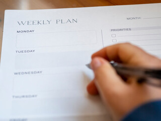 Woman's hand-holding pen and weekly planning on a blank daily schedule. Week planner for...