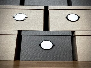 close-up of boxes with blank white labels stacked in a row on top of each other.  Lots of storage boxes made of fabric in dark and light colors close up. Home box storage system close up.