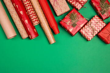 Christmas preparations with gift boxes and wrapping paper on on green background.