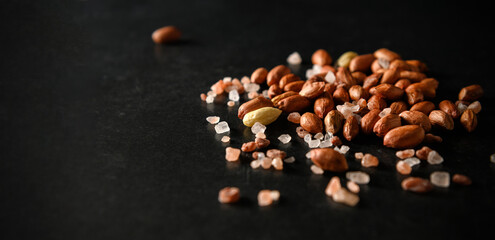peanuts, dry groundnuts, with Himalayan coarse salt on dark gray background, banner, space for text