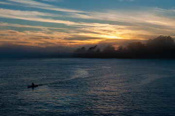 Obraz premium Silhoutte of a person in a kayak peddling in the Santa Cruz bay during sunset.